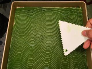 波浪抹茶蛋糕卷,拿一块锯齿刮刀，在抹茶蛋糕糊上画好波浪纹，冰箱冷藏备用