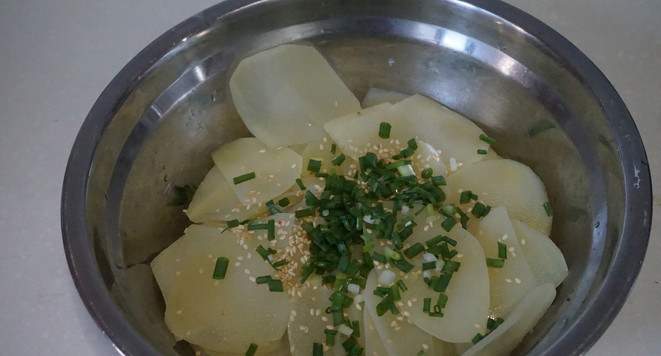 响油土豆片,焯好的土豆捞起盆内，加入白芝麻和葱花。