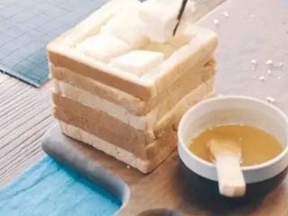 蜂蜜厚士多,挖出的吐司切成四方块，往面包框中填放，每填一层，刷一道黄油蜂蜜溶解液。