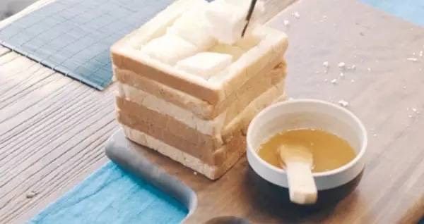 蜂蜜厚士多,挖出的吐司切成四方块，往面包框中填放，每填一层，刷一道黄油蜂蜜溶解液。