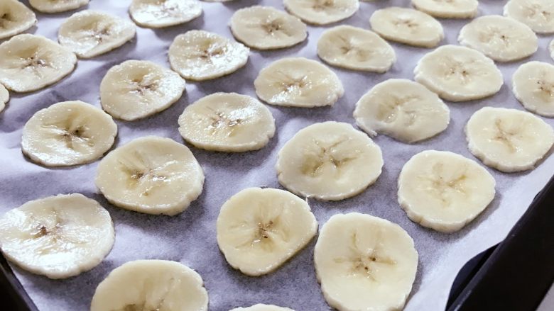 宝宝辅食：烤香蕉片-18M ,烤盘中垫涂层油纸，最好是油布，才不会黏住撕不下来哈。将切好的香蕉薄片均匀码在烤盘上。
