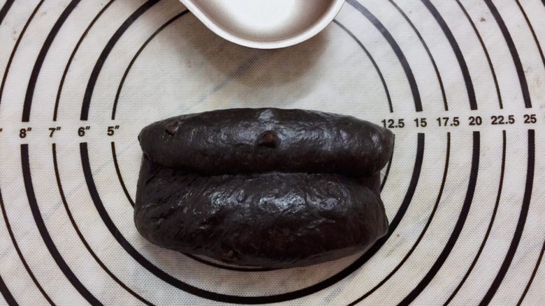黑可可热狗包,取一小份面团，擀成椭圆形，两边向中间卷起，收口捏紧，搓成橄榄形