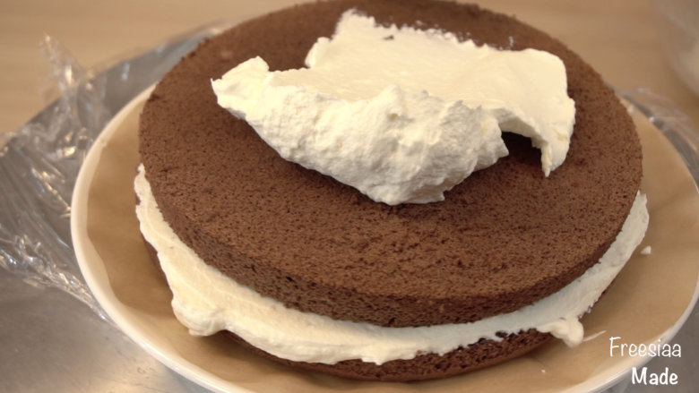 可可戚风 巧克力围边奶油蛋糕（视频菜谱）,将蛋糕的烘烤面放最下层，涂上一层奶油，四周可以稍微溢出来些，再放上第二层蛋糕（烘烤时的底层做顶部），再涂上奶油
