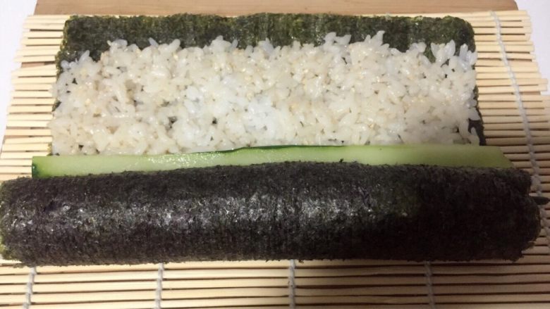 酱香味秋葵寿司（纯素版）,打开竹席放一根黄瓜条，用竹席继续卷
