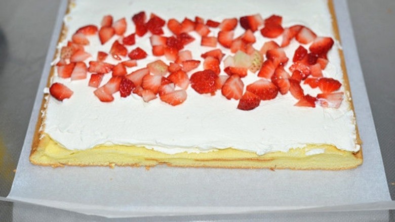 草莓奶油蛋糕卷, 蛋糕片上涂上打发好的淡奶油，涂的时候要前端厚后端薄，均匀地撒上草莓粒，用擀面杖包着油纸将蛋糕卷卷起来，冰箱里冷藏二个小时，定型后切片即可。