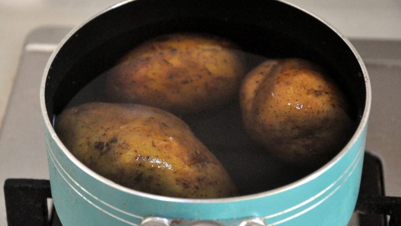 芝士焗香肠时蔬土豆泥,土豆洗净后连皮放入小奶锅中，水没过土豆，开大火将水煮沸后再转中火煮20分钟，筷子戳进去即熟透。