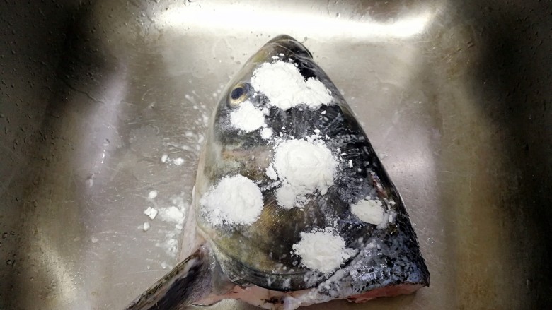 剁椒鱼头（低辣版）,取适量生粉在鱼头表面抹匀，再用清水冲洗干净。