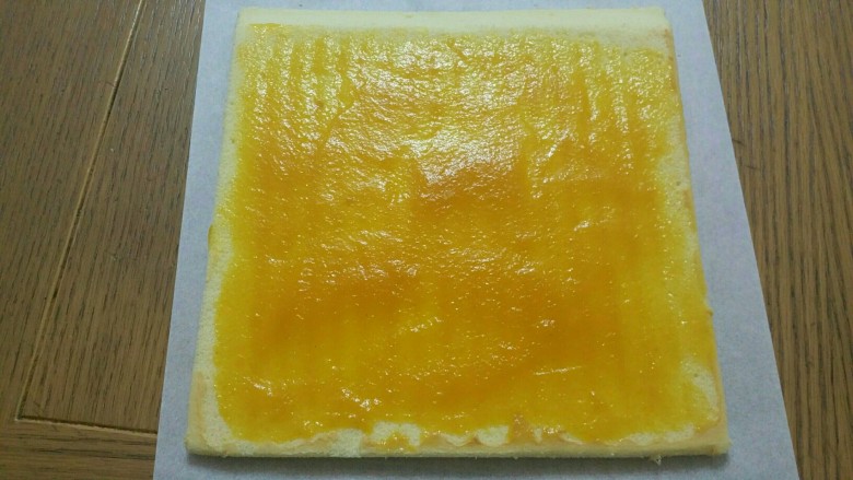 香芒果酱蛋糕卷,桌子上放一张新油纸，蛋糕毛巾面朝下，撕去上面的油纸，斜切蛋糕一边，抹上自制的百香果芒果果酱