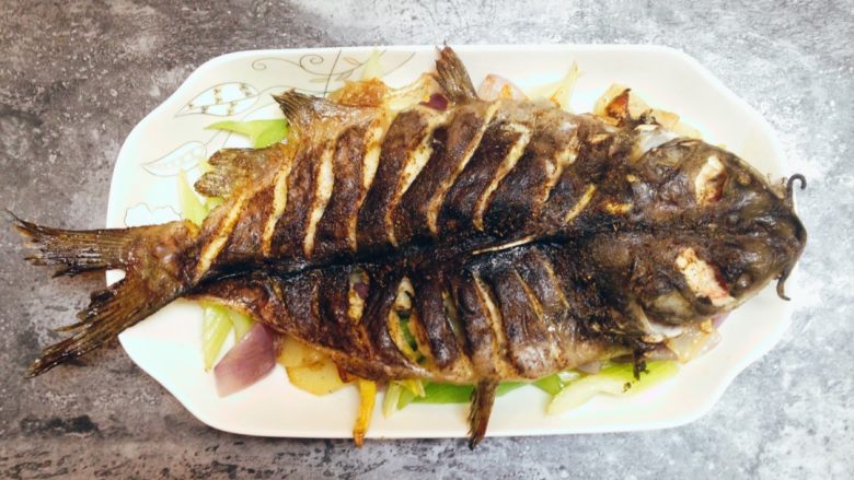 香辣烤鱼,将烤好的鱼移入鱼盘，鱼背向上铺放在炒好的菜上面。