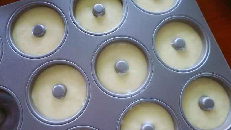 椰香甜甜圈（烤箱版）,面糊挤进模具中，约8分满，轻轻敲几下烤盘震荡出大气泡，模具中一个甜甜圈的直径为7cm，配方能制作9个的量。