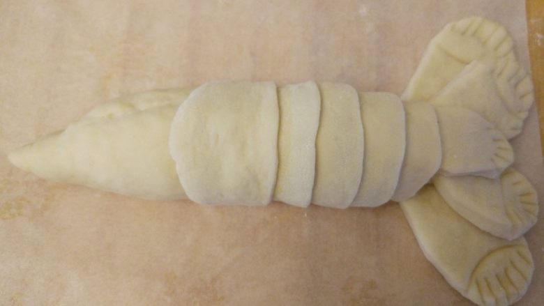龙虾面包,制作身体的壳：再取一块面团，揉成长条，切成剂子，擀薄成圆片后对半切开，一片压一片，按照小龙虾外壳的样子包好。中间用少许蛋液粘合
