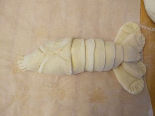 龙虾面包,制作头部：同理，擀一大块面片，一端切三角形，包住头部，用手捏出花纹