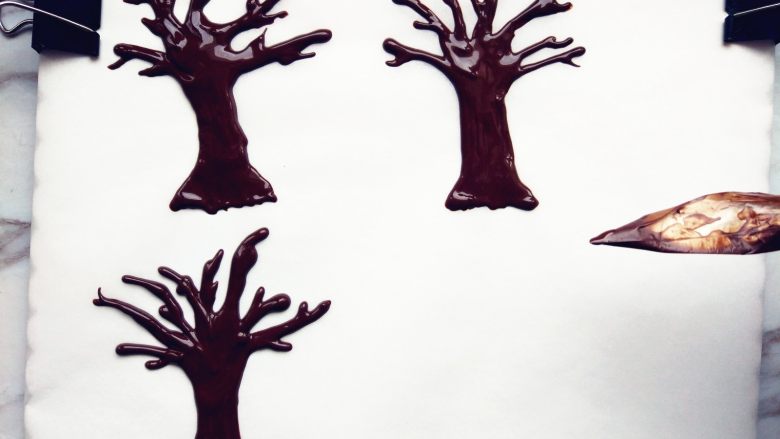 雪国的树——椰蓉巧克力杯蛋糕,裱花袋剪小口，在油纸上随意画出树的形状。也可以在油纸背面提前画出草稿，树干底部稍长稍粗壮一些，因为要插入杯蛋糕中