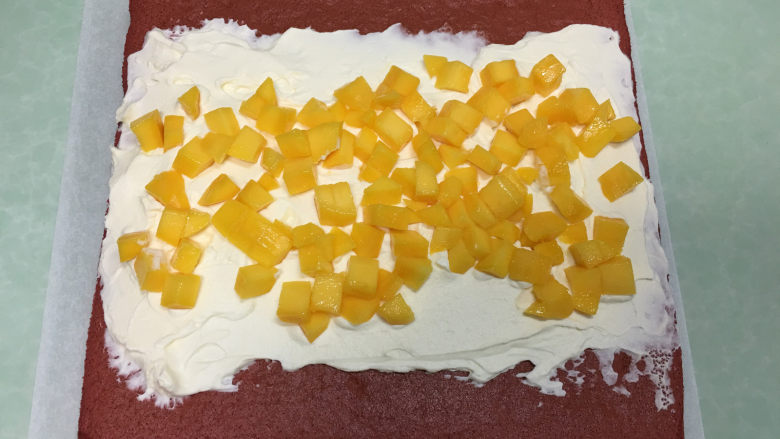 红丝绒蛋糕卷,蛋糕凉了以后在蛋糕表面涂上打发好的奶油，铺上芒果丁。