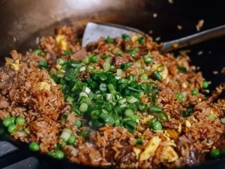 牛肉炒米饭,待米饭炒热后调入适量盐，酱油，最后撒上，青豆，小葱花炒均即可出锅。