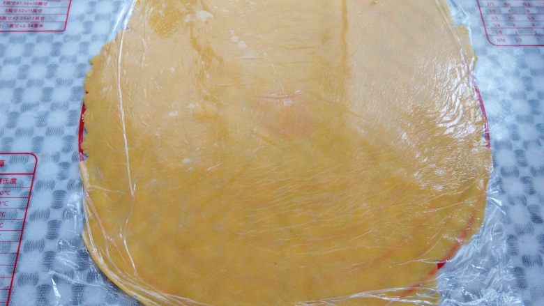椰香南瓜派,面团取出，上下垫一层保鲜膜，用擀面杖擀成一张大饼皮，要比派盘直径大一圈