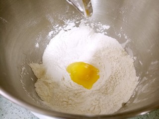 椰蓉花卷面包,在面粉中间挖个坑，打入鸡蛋，搅拌均匀。