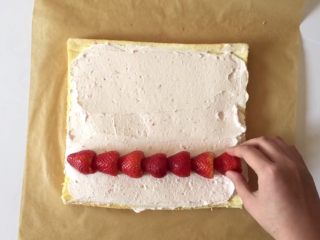草莓三重奏蛋糕卷,将打发好的淡奶油抹在蛋糕上，均匀的摆上草莓