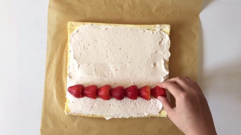 草莓三重奏蛋糕卷,将打发好的淡奶油抹在蛋糕上，均匀的摆上草莓