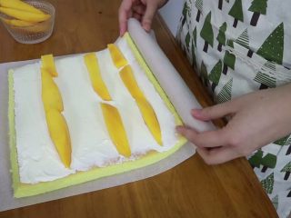 芒果分蛋海绵蛋糕卷,在晾凉的蛋糕片上涂抹上打发的淡奶油，摆上三条均匀的芒果，借助擀面棍卷起来