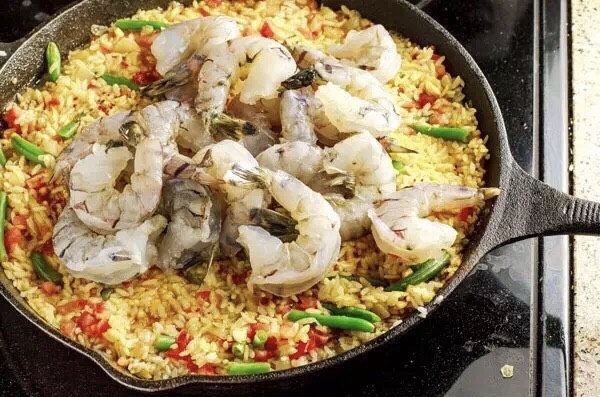 简易版西班牙海鲜饭,开盖，均匀摆入去壳和虾线的大虾，如需加水可少量添加，扣盖再焖煮10~15分钟。