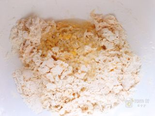 咸香芝麻饼,戴上一次性手套将鸡蛋和面粉混合成颗粒状后，倒入温水，继续戴上手套揉匀。