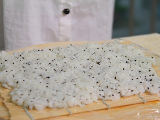 自制寿司,寿司帘上铺上保鲜膜，折到竹帘下面方便拉伸，再盖上米饭并且用勺子压实（勺子沾纯净水可以防粘哦）
