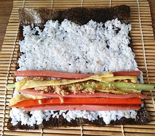 什锦火腿寿司,将饭团往四周推平，在下端摆放蛋皮、黄瓜、火腿、肉松和胡萝卜