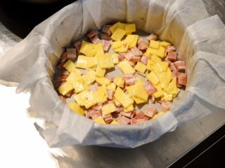 法式咸派【魔法蛋糕】,到这一步就可以烤箱160℃开始预热了。将我们切好的奶酪和培根片均匀的铺在底部。模具里一定要铺油纸。