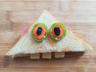 百变大眼怪三明治,盖上吐司片，装饰上青椒圈做的眼睛，放上2颗黑加仑做眼珠