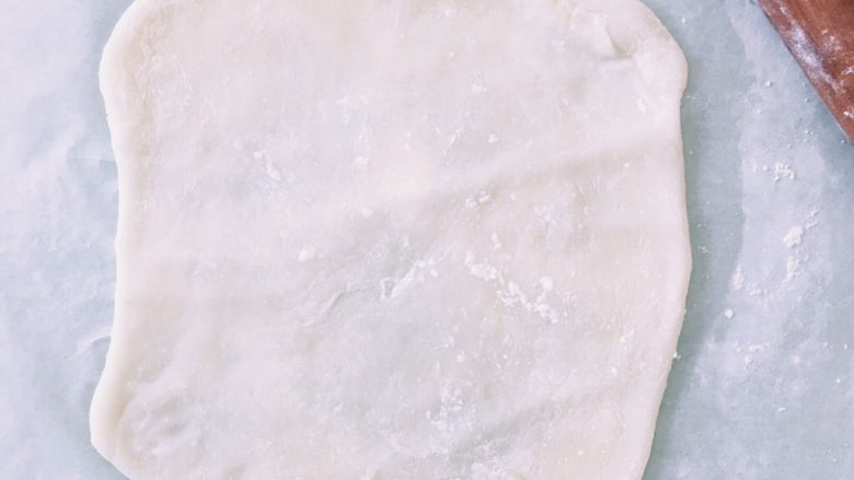 抹茶白玉卷,把卷皮放在油纸上，表面也洒少量的玉米淀粉防止过粘，用擀面杖擀成长方形，长度约要是要卷蛋糕体长度的5倍