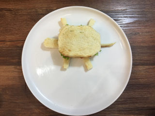 童趣早餐——乌龟全麦三明治,用切剩下的面包边角料切出乌龟的头、脚和尾巴，摆放在乌龟的身体旁边。