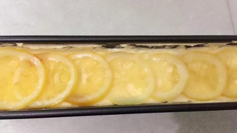檸檬奶酪磅蛋糕,倒入模具中 離台面用力敲幾下 消除部分氣泡 將麵糊抹至兩邊高 中間低 表面鋪上蜜漬檸檬片送入已預熱170度的烤箱中烤約50分鐘