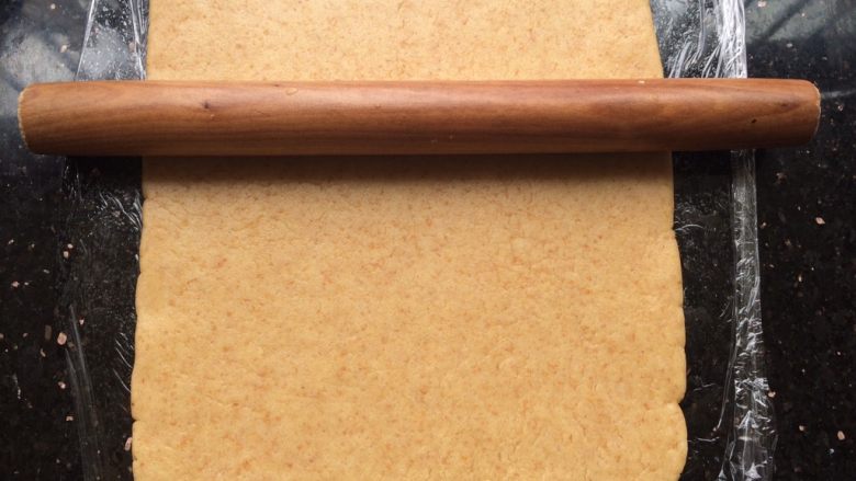 黑米年轮小卷饼干,操作台上贴一张保鲜膜，把面团放上用擀面杖擀开成长方形状。