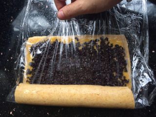 黑米年轮小卷饼干,先卷起一点，然后拿起保鲜膜往一头拉卷起成圆柱形。