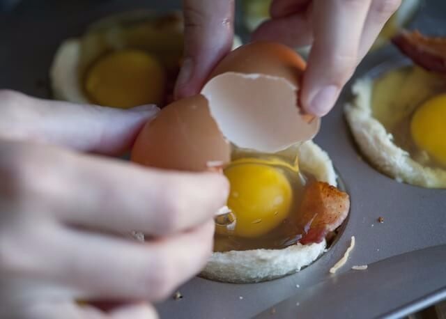 培根，鸡蛋和烤面包杯,每个松饼杯加一个大蛋。根据蛋的大小，一些白色可能会耗尽，只需使用纸巾清洁每个松饼杯周围，以确保蛋杯一旦烘烤即可轻松取出。