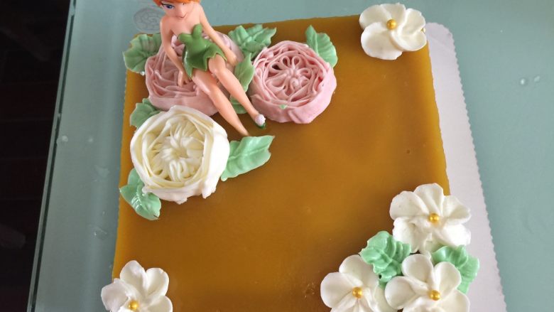 花仙子芒果慕斯,把提前用奶油霜裱好的花和花仙子人偶都放在蛋糕上面装饰，再用奶油霜挤上叶子即可