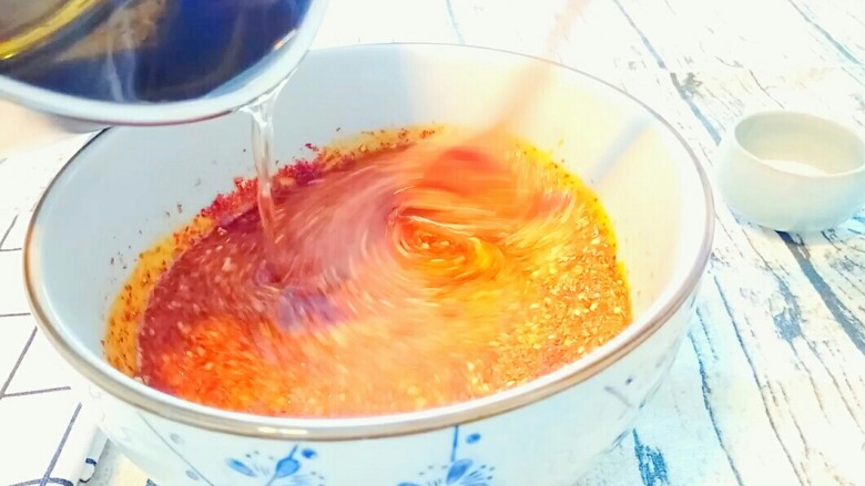 自制油辣子,端起小奶锅，将油慢慢倒进辣椒面，同时另一只手拿勺子搅拌辣椒面。直至油全部倒进去。