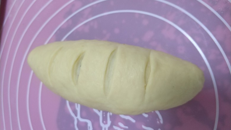 坚果面包#面团的发酵之旅#,从一端卷起，整形成橄榄球状，捏紧收口，用锋利的刀在上面切几个小口子