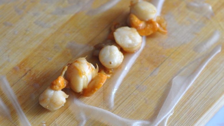 扇贝越南春卷,将软掉的米粉皮铺平，扇贝肉放在中间，排成一排。