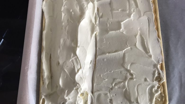 哆啦A梦彩绘蛋糕卷,淡奶油抹在蛋糕片上。因为做e型卷，所以左手边将淡奶油堆成小山丘，用擀面杖和油纸辅助，将蛋糕卷卷起。