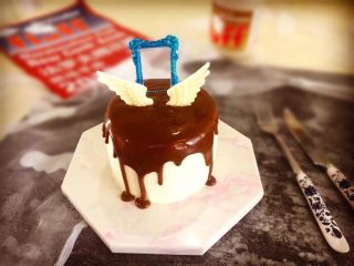 【天使之城】巧克力淋面蛋糕,冷藏的蛋糕取出，淋上放至手温的巧克力淋面酱，再放上白巧克力装饰就0k了。(食用银粉中加入蓝色食用色素调匀，刷在白巧克力装饰框的表面放入冰箱冷冻2分钟取出放在蛋糕上就0k了）