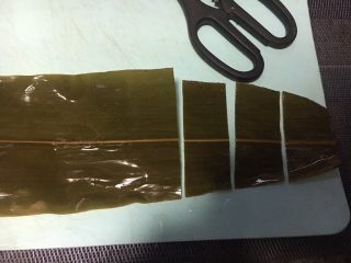 五彩糯米排骨卷,粽叶铺平，从三分之一处剪成三段，舍弃最顶端不要，剪的宽度和小排的宽度相同