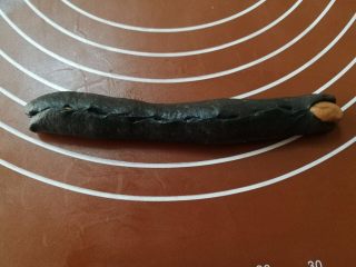 豹纹吐司,7.取一个黑色竹炭面团，擀成椭圆形的面片，大概15厘米长，包住刚刚搓好的咖啡色长条，可以全包住也可以只包住咖啡色面团的三分之二。