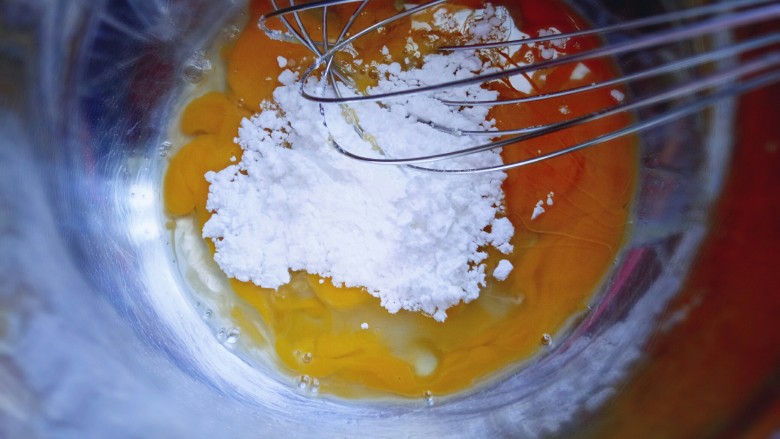 芒果千层蛋糕,把鸡蛋敲在容器里，加入糖粉，用手动打蛋器搅拌均匀。