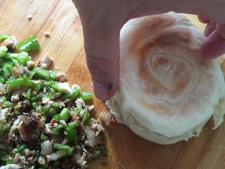 肉夹馍,烙好的饼用刀从中间剖开，放入剁碎的肉和青椒。勺子舀少许煮好的肉汤浇上去。