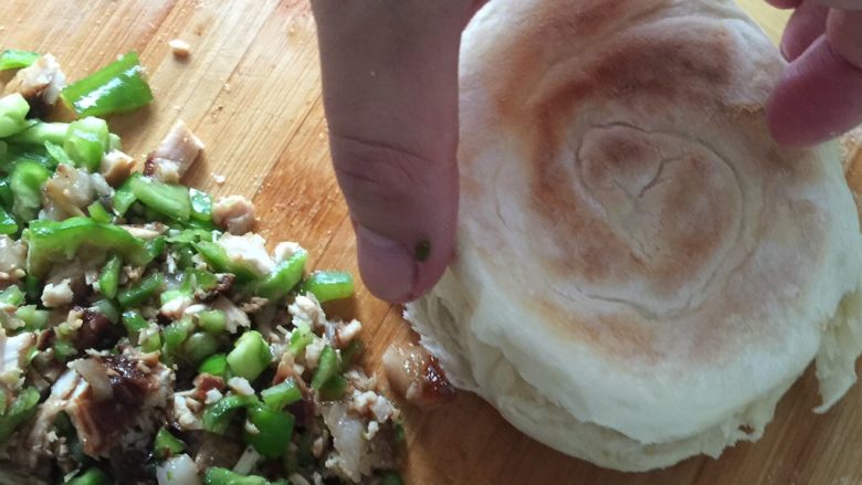 肉夹馍,烙好的饼用刀从中间剖开，放入剁碎的肉和青椒。勺子舀少许煮好的肉汤浇上去。