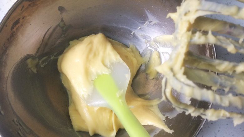 流心泡芙玛芬,转而用电动打蛋器，慢速搅打面糊，慢慢加入剩余的蛋液。搅打后的面糊用刮刀再拌匀，面糊富有光泽。