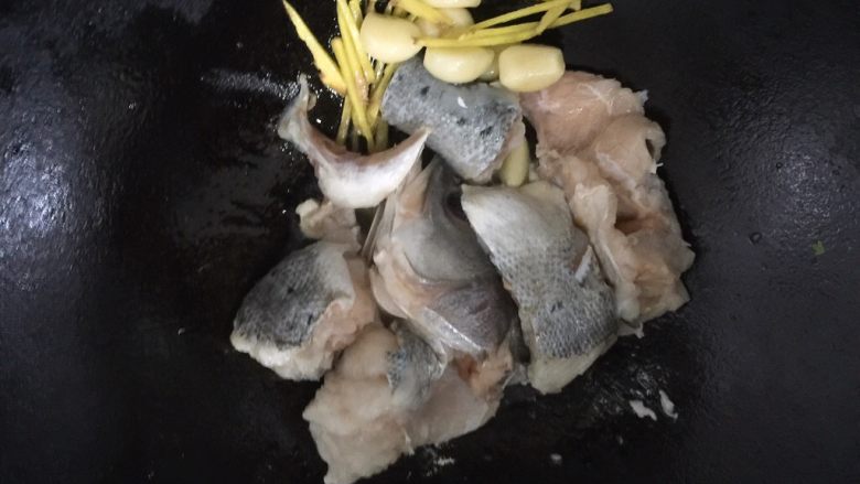 酱烧海鲈鱼,把姜丝和蒜瓣撇一边去，依旧中火，放鱼段下锅煎制。几分钟后翻下面，锅内油多的话外皮呈金黄色时即可。