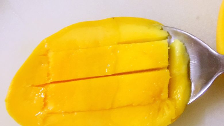 夏日冰爽黄瓜芒果卷,用不锈钢勺子沿着果皮挖进